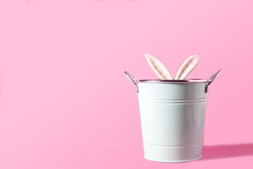 Modern Easter concept. Ears of bunny or rabbit in blue bucket on pastel pink background. Selective focus. Spring postcard. Copy space.