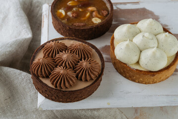 Mini chocolate cakes on wooden background. In the background is a cake with Cashew nut filling, almonds, peanuts.