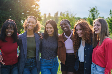 Group of young women with different cultures together outdoors at sunset in a park