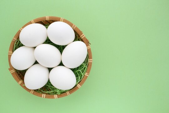 Fresh chicken eggs in wooden rattan wicker basket on green background. Natural healthy nutrition organic farm food product concept. World egg day, easter holiday composition. Close-up, flatlay