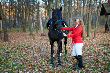 Young sexy woman standing near a horse in a red suit. Beautiful  professional female jockey...