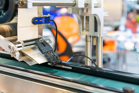 Close up fur brush and label paper of automatic continuous sticker labeling machine for labelling product on belt conveyor in manufacturing process in industrial