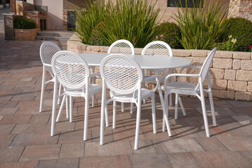 white metal table with 6 white plastic chairs in the garden of the house, elegant luxury
