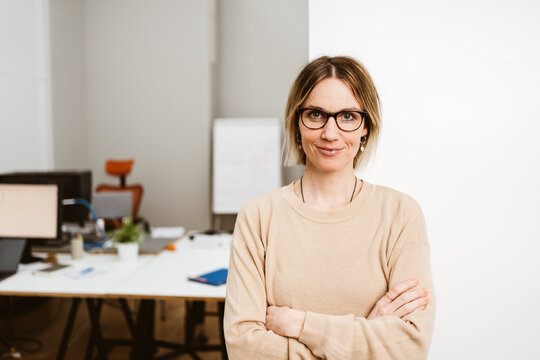 Young business woman leaning against office wall and looking at camera