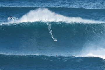 Surfer is riding a giant big wave in Nazare, Portugal. Biggest waves in the world. Touristic destination for surfing and lovers of radical sports. Jet skis in the water. Amazing destinations.