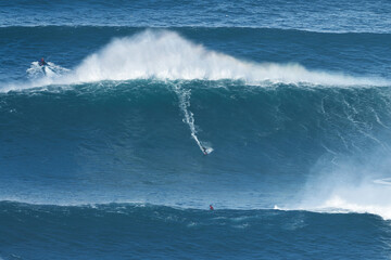 Surfer is riding a giant big wave in Nazare, Portugal. Biggest waves in the world. Touristic...