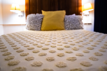 Throw decorative pillows, tufted comforter duvet on bedroom bed with soft cover in evening with modern bedside lamps illuminated in hotel or home