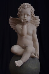 A marble angel with wings sits on a round stone and blows a kiss