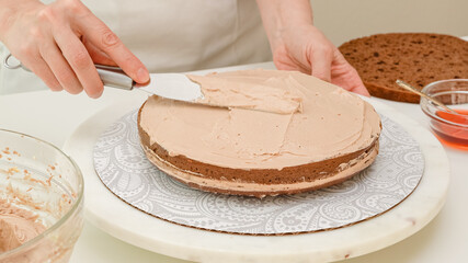 Assembling the cake. Woman hands topping part of the cake with chocolate cream. Step by step chocolate cake recipe