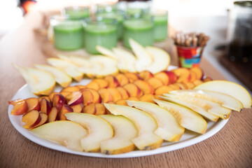 Large healthy plate with various cut fruits (plums and melon) and green juices