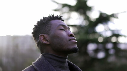 African man taking a deep breath outside at park. Close-up person meditating