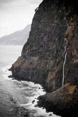 Madeira island landscape of Véu da Noiva or Bridal Veil waterfall flowing from the rocks into the ocean and seen from the viewpoint above. Toned image with desaturated colors and vertical orientation