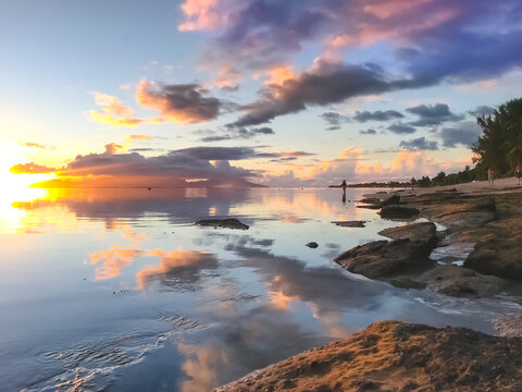 Bright tropial sunset reflected in ocean water. Colorful clouds in sky and rocky seashore. Amazing natural summer scenery. Wonderful Nature landscape during sunset. Travel, tourism, relax. © Anastasia Pro