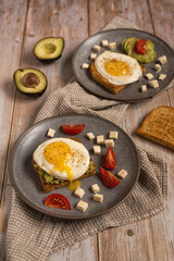 Avocado toast. Healthy breakfast for two: toast bread with fried eggs, avocado, feta cheese and tomato in ceramic plates on a wooden table. Healthy food. Healthy lifestyle.