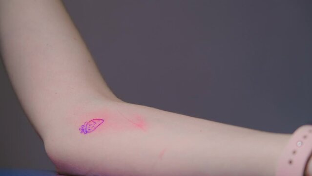 Tattoo master makes a tattoo on the client's hand. Hand poke tattoo. Small strawberry tattoo. Tattoo artist makes hand poke tattoo