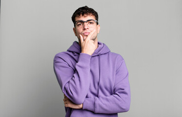 looking serious, thoughtful and distrustful, with one arm crossed and hand on chin, weighting...