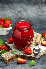 A jar of strawberry jam on a wooden board, vertical image. top view. place for text