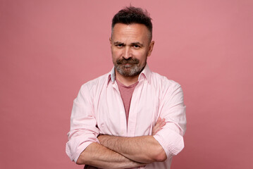 Mature handsome man with beard and mustache dressed in pink pastel shirt with crossed hands...