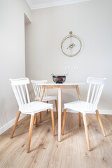Round kitchen table and four white chairs with natural wood legs. White walls and natural wood floors