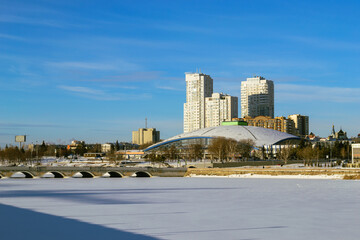 Fototapeta na wymiar Panorama of a frozen river and buildings illuminated by the sun on a winter day against a blue sky