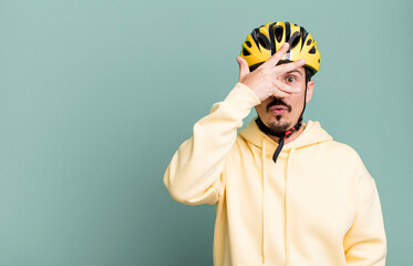 adult man looking shocked, scared or terrified, covering face with hand. bike helmet and bicycle...