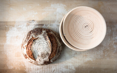 Single round loaf of crusty baked sourdough bread on lightly floured blonde wood board with coiled...