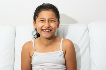 portrait of latin brunette girl, sitting on the sofa smiling and showing her teeth, girl with...