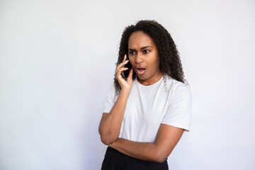 Portrait of indignant young woman talking on mobile phone over white background. African American...