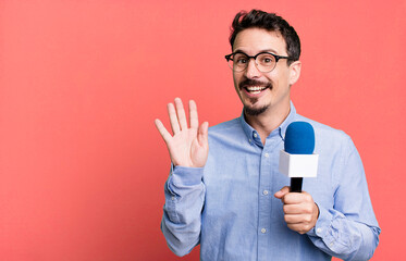 adult man smiling happily, waving hand, welcoming and greeting you with a microphone. presenter or...