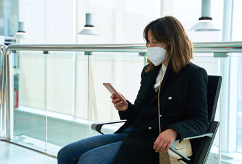 pretty brunette girl with protective mask looks at the mobile sitting in a station