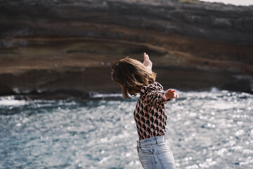 carefree girl opens her arms while walking along a cliff