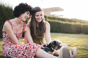 A young lesbian couple play with a dog. Girls have fun with a yorkshire on the lawn. LGTBI concept, lifestyle.