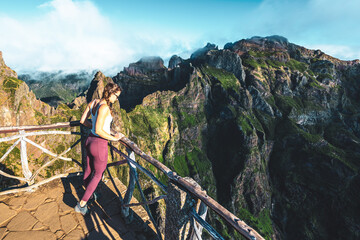 Woman enjoying the mountain scenery of Pico Ruivo from a viewing platform with very steep cliff in...