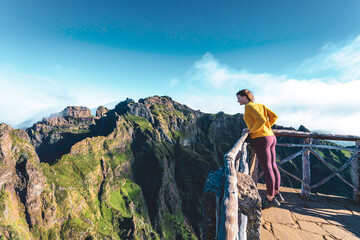 Woman enjoying the mountain scenery of Pico Ruivo from a viewing platform with very steep cliff in...