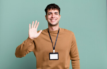 adult man smiling happily, waving hand, welcoming and greeting you with an acccess identity card