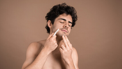 A young caucasian man with stubble beard is doing a facial massage using a Gua Sha