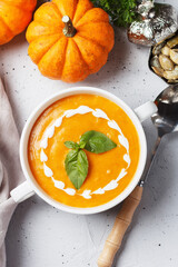 Cream soup of baked pumpkin and carrots with cream and pumpkin seeds with herbs on a gray background. Vegan food.Vertical photo