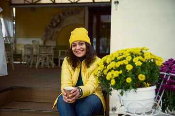 Attractive woman in yellow hat and jacket, smiling a toothy smile looking at camera, sitting on the...