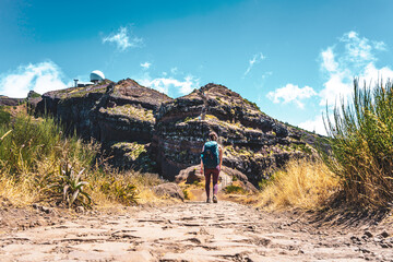 Naklejka premium Sportive woman with backpack walking along scenic hike trail to Pico do Ariero in the afternoon. Verade do Pico Ruivo, Madeira Island, Portugal, Europe.