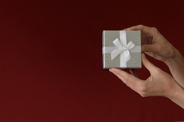 Time for Gifts  A woman hand holds a gift box on a red-burgundy background. Minimalism. copy space