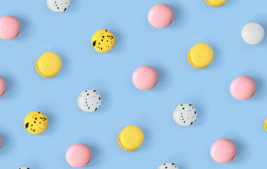 Many different macaroons pattern on blue background. Pink, white and yellow French cookies. Strawberry, black currant and blueberry, lemon and lime vanilla meringue dessert