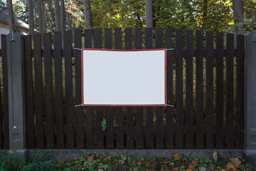 Blank white banner in red frame mounted on wooden fence outdoor. Street advertising and business...