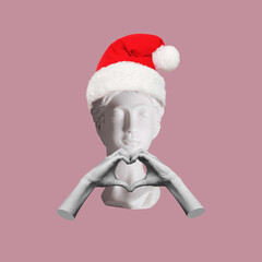 Female antique statue's bust in Santa hat on her head showing heart shape with hands on pink color background. Trendy collage in magazine surreal style. 3d contemporary art. Modern design. Christmas