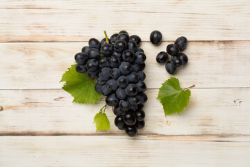 Bunch of ripe dark blue grapes with leaves on wooden background, top view
