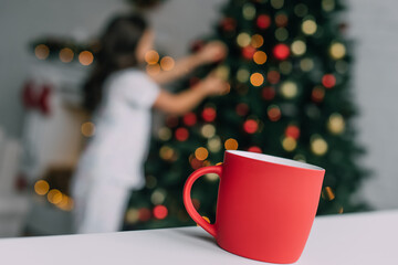 Red cup on table near blurred girl and Christmas tree at home