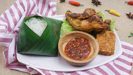 Indonesian Grilled chicken breast on white plate. It served with rice, sambal, fried tempeh and lettuce