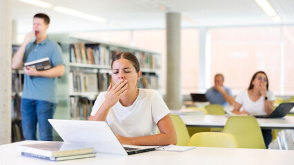 Female student yawns out of boredom in the public library