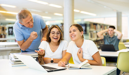 Mature librarian male bringing the index finger to the mouth to a group of laughing students in the library