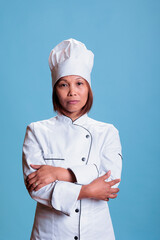 Elderly cheerful chef standing with arm crossed in studio preparing culinary recipe using healthy...