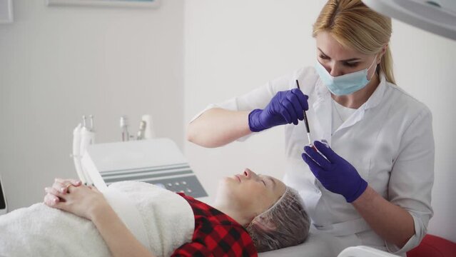A female cosmetologist smoothes out wrinkles with microcurrent. Rejuvenating facial treatment. A girl receives a lifting therapeutic massage in a beauty spa. Cosmetology clinic, procedures.